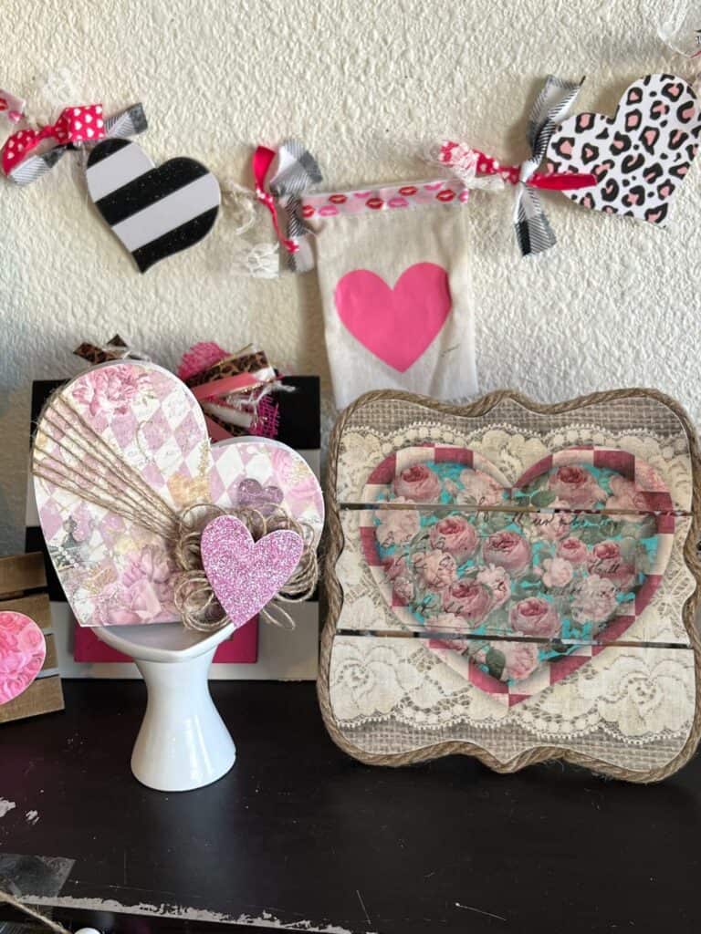 The dollar tree heart with glamentine printable on it sitting on a heart riser next to a vintage heart pallet board decor.