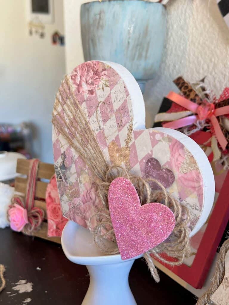 close up of the completed project showing the twine circular loopy bow and the pink glitter heart.