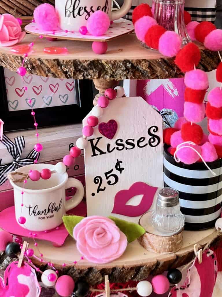 White wood hangtag that says kisses 25 cents next to a mini mug that says thankful and a pink felt rose in the front.