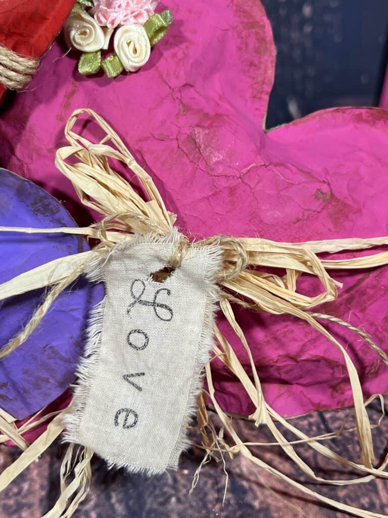 I piece of muslin with frayed edges and the word "love" stamped on it, hanging from a raffia bow.