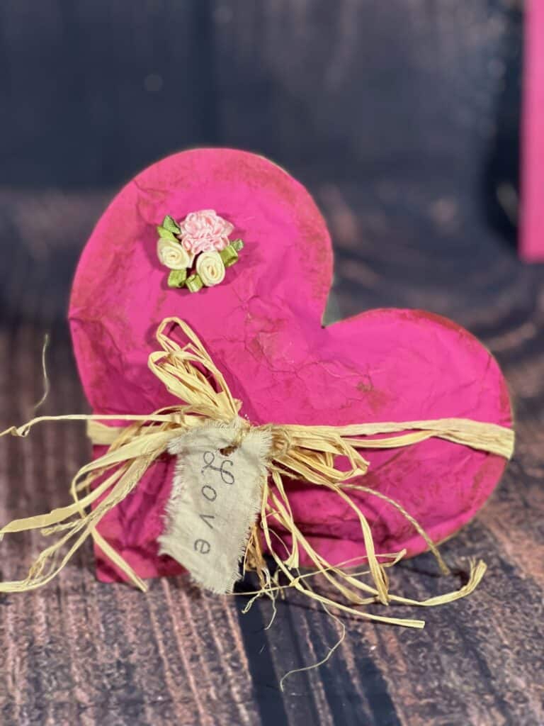 The completed pink kraft paper heart with the LOVE hangtag and a raffia bow with creme and pink silk roses.