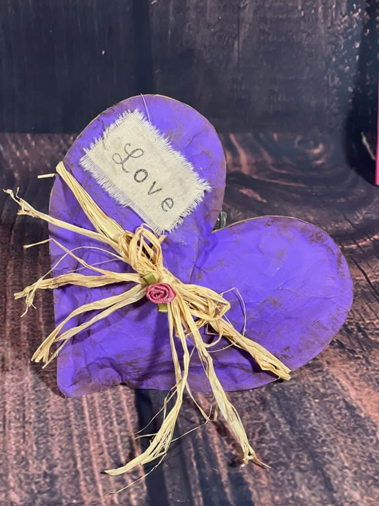 The completed purple kraft paper heart with the LOVE patch and a raffia bow with purple silk rose.