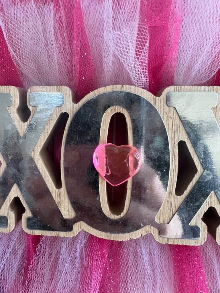 Pink heart embellishment in the middle of the O in the XOXO word.