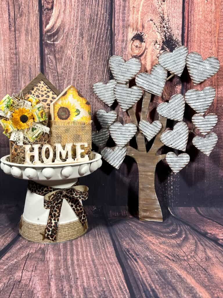 A white riser with leopard bow with sunflower and leopard house decor on top. The completed cardboard faux metal tree on the right with e faux wood backdrop.