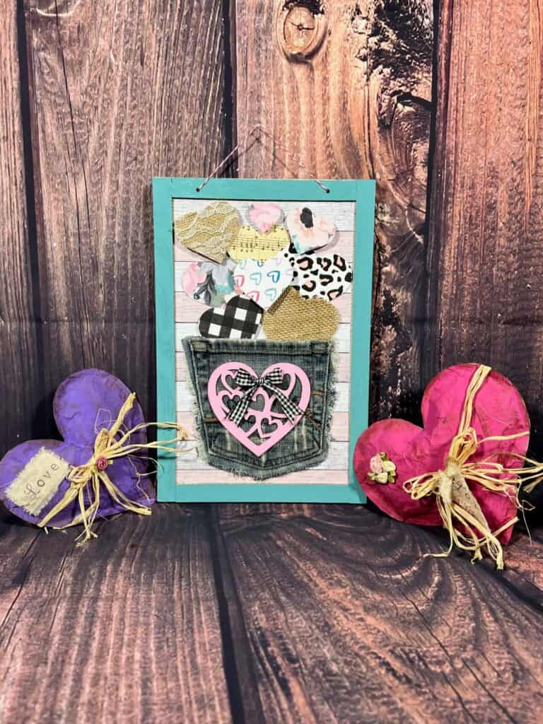 The completed jeans pocket heart sign hanging in between two kraft paper hearts, one pink one purple.