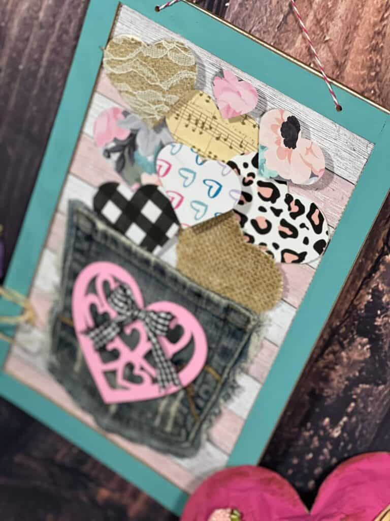 Jeans Pocket Valentines Day DIY Heart Decor with a dollar tree pink heart cutout, buffalo check bow, and small hearts floating out of the pocket with burlap, lace, and other scrapbook paper hearts.