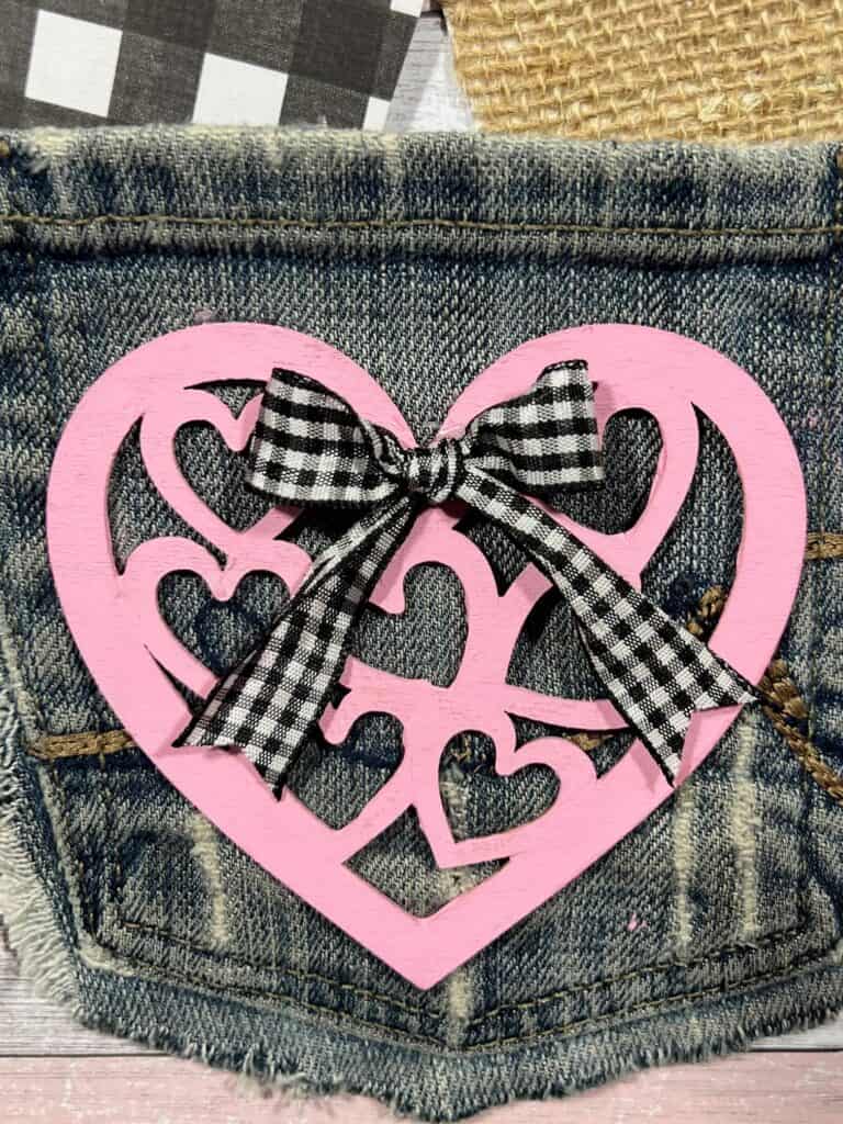 Small wood ordained heart cutout painted pink with a buffalo check bow.