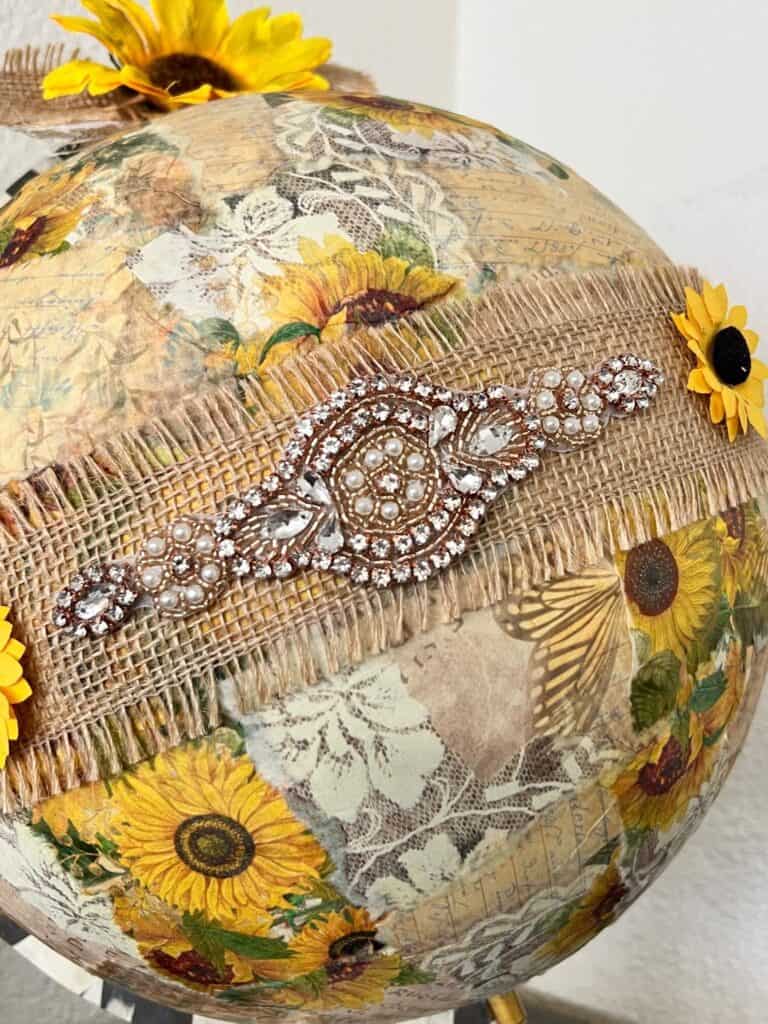 The center of the globe with burlp ribbon and a rhinestone applique, with a small sunflower on each side.