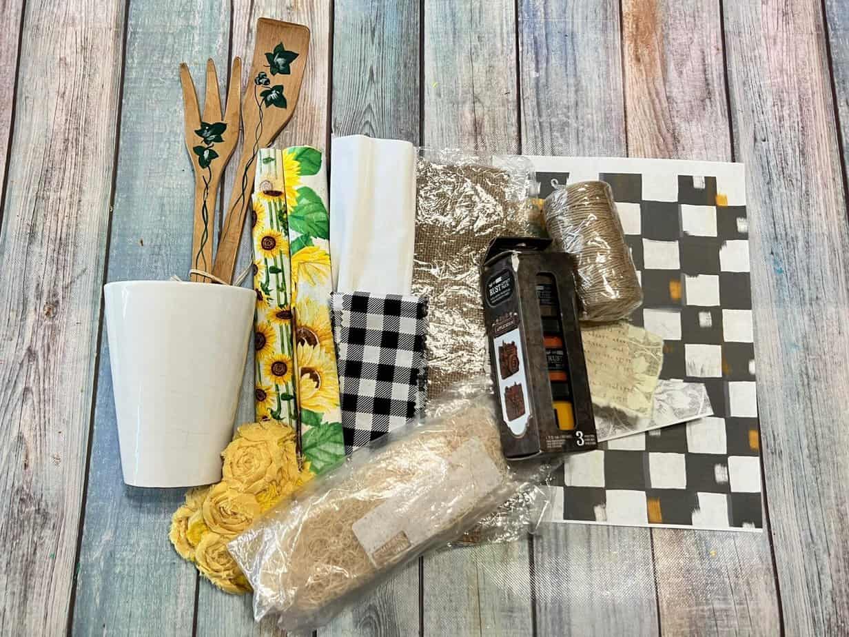 Supplies needed to make the rusted utensil kitchen jar decor with a glass vase, wood utensils, rust effect paste, and rice paper printables.