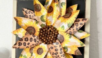 Scrapbook paper sunflower DIY home decor with leopard print flowers on a wood surface with wood bead center and a wire hanger.