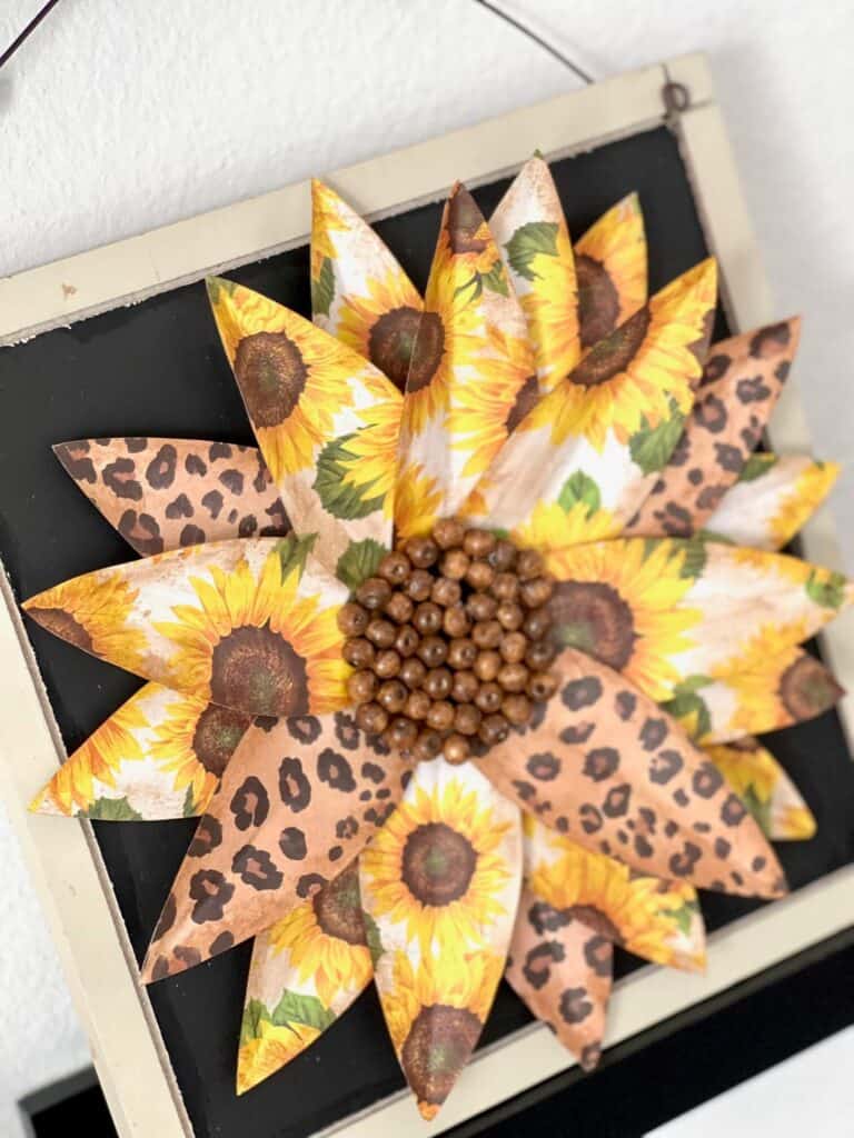 Scrapbook paper sunflower DIY home decor with leopard print flowers on a wood surface with wood bead center and a wire hanger.