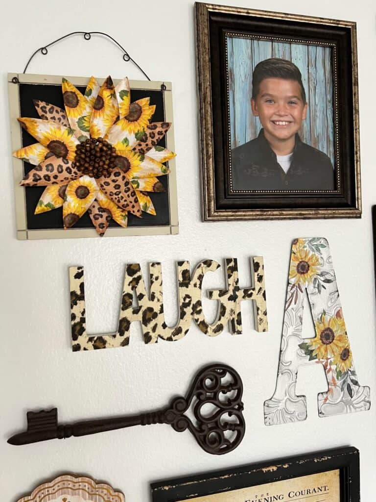The scrapbook paper sunflower hanging on a gallery wall above a leopard print word "laugh" a cast iron skeleton key and a sunflower letter "A".