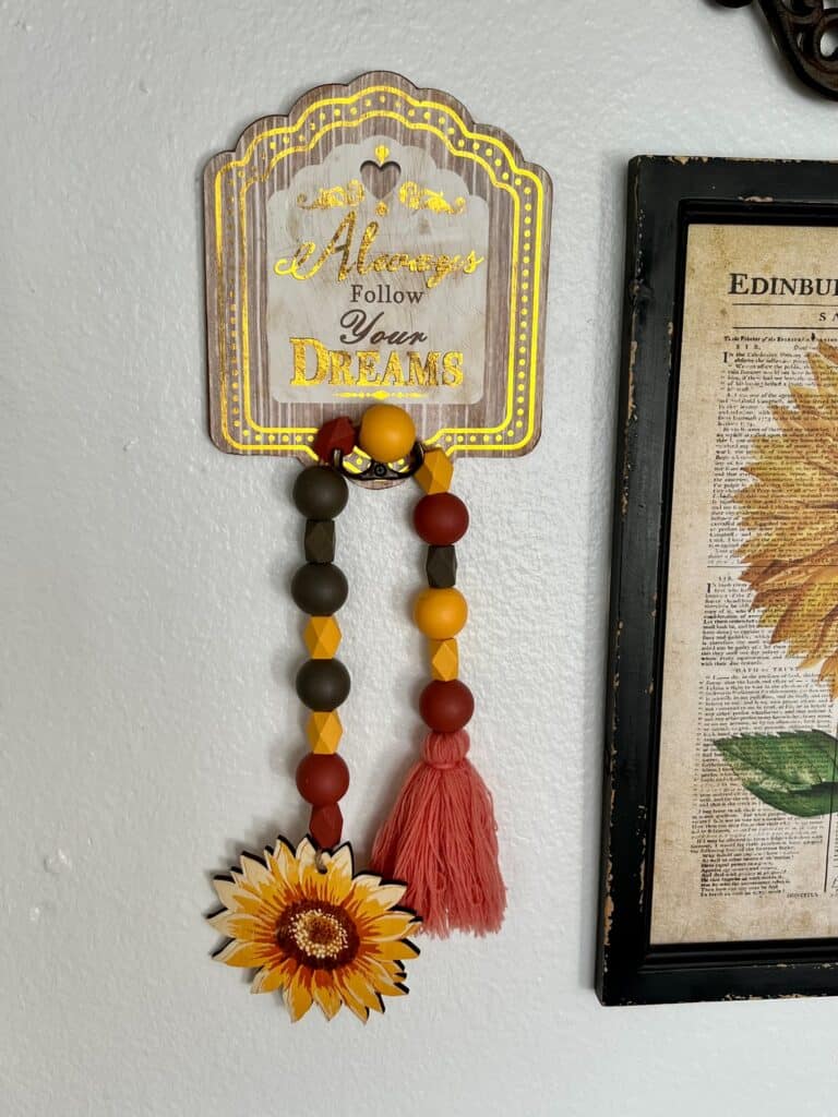A decor hook that says "Always follow your dreams" with a sunflower wood bead garland hanging from it.