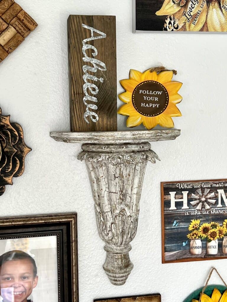 A crackle wooden shelf with a block that says "Achieve" and a small sunflower that says "Follow your happy".