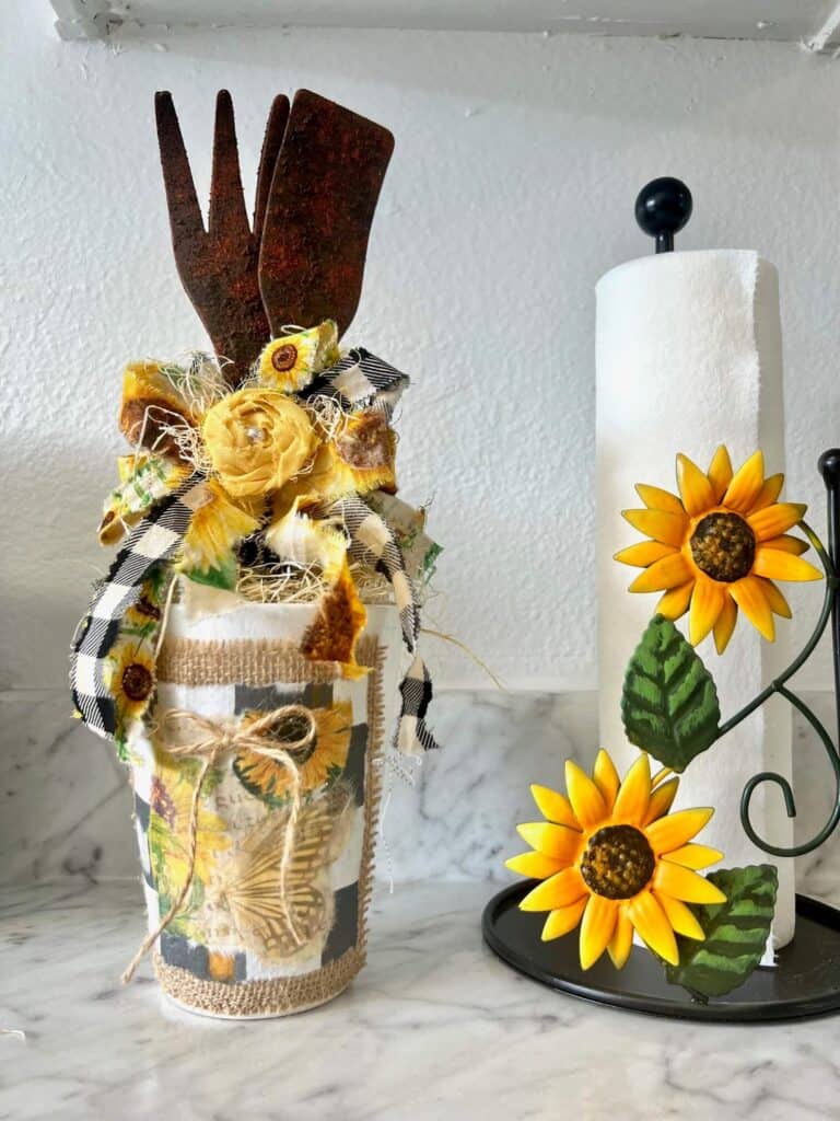 Rusted utensil jar with a big sunflower bow on the kitchen counter next to a sunflower paper towel holder.