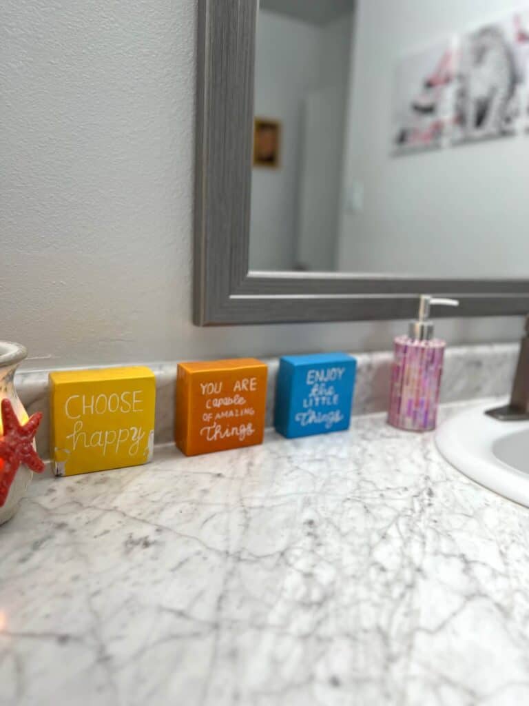 3 ceramic blocks that have a saying on each. one orange, one blue, and one yellow.