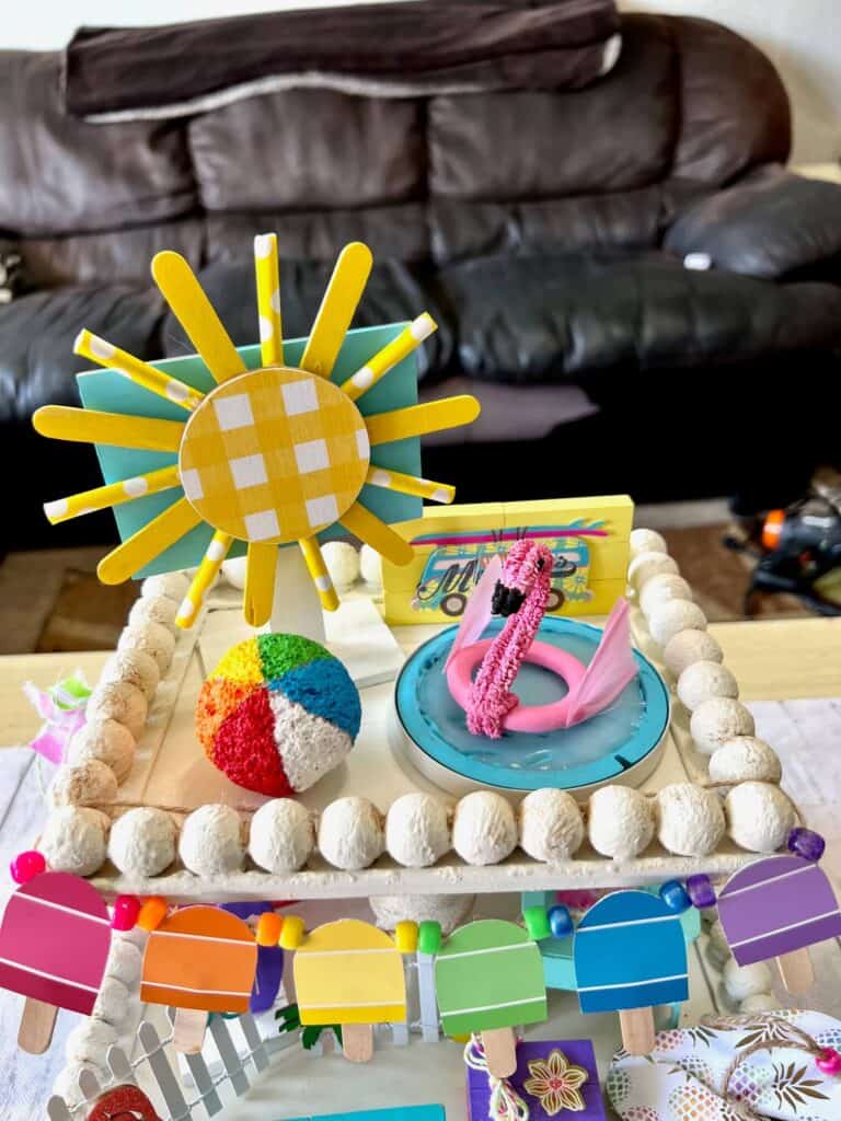 The top tier of the tray showing the popsicle stick sun, flamingo floaty and hot glue pool, and styrofoam beach ball.