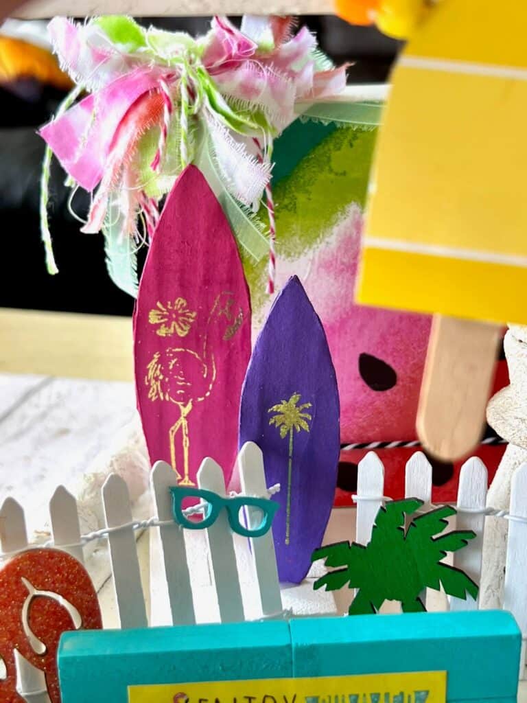 Small cardboard standing surfboards. One pink and one purple. 