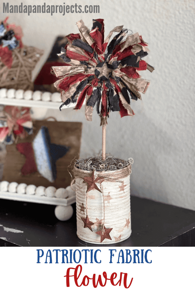 Patriotic Fabric Ring Flower with a recycled tin can base painted white with antique wax stars, twine and a rusty star made with red white and blue American flag fabric and dollar tree wood ring center. Rustic 4th of july DIY Decor.