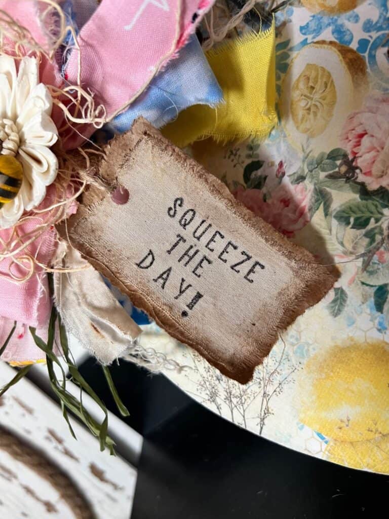 A hangtag made with kraft paper and muslin that has the phrase "squeeze the day" stamped on it.