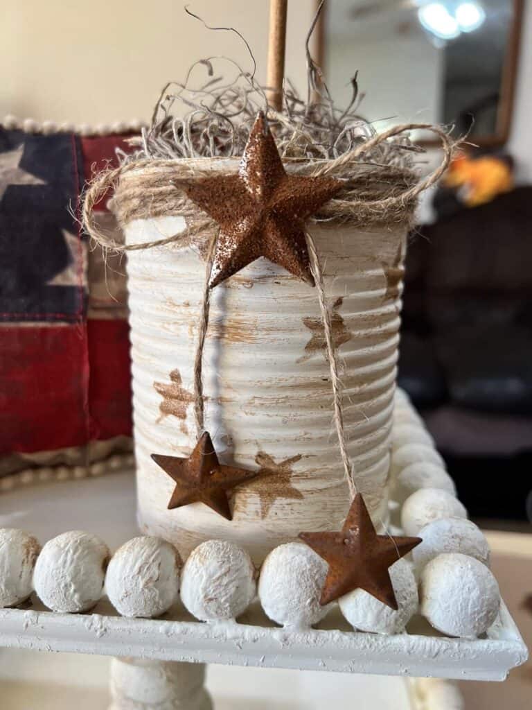Recycled tin can painted white with antique wax stars with twine on the top and rusty stars.