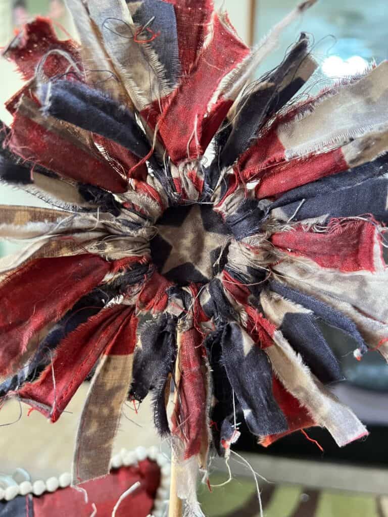 The top part of the fabric flower with the american flag fabric strips tied around the wood ring and a rustic star center.