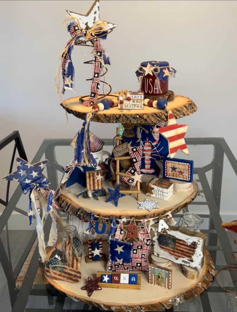 Patriotic Rustic Tiered Tray decorated with handmade mini 4th of july americana crafts and DIY decor on all 3 tiers of the large wooden round tray. Red white and blue crafts and decor.