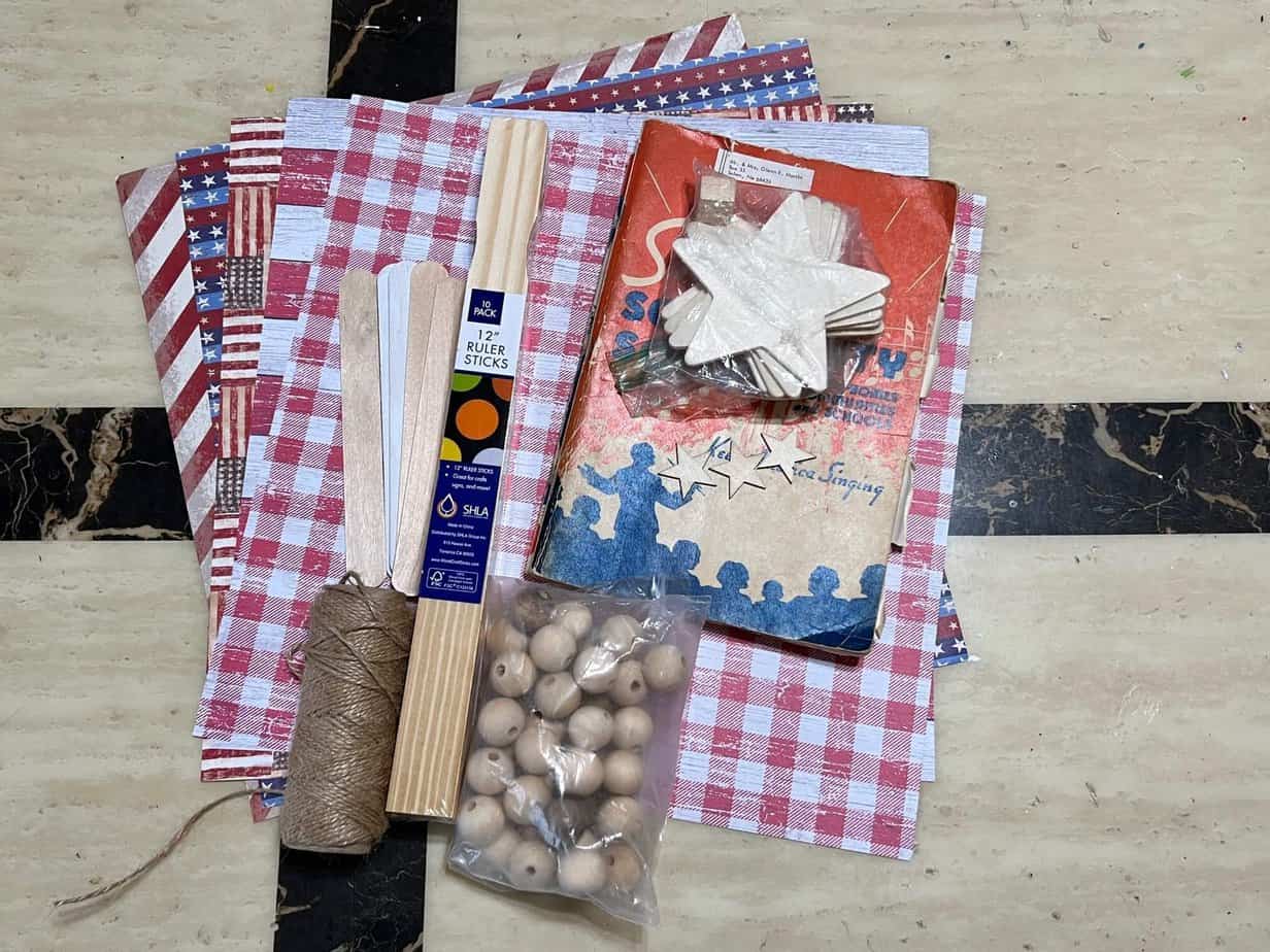 All of the supplies needed to make the craft laid out on the table. Scrapbook paper, twine, wood beads, and music sheet paper along with wood stars.