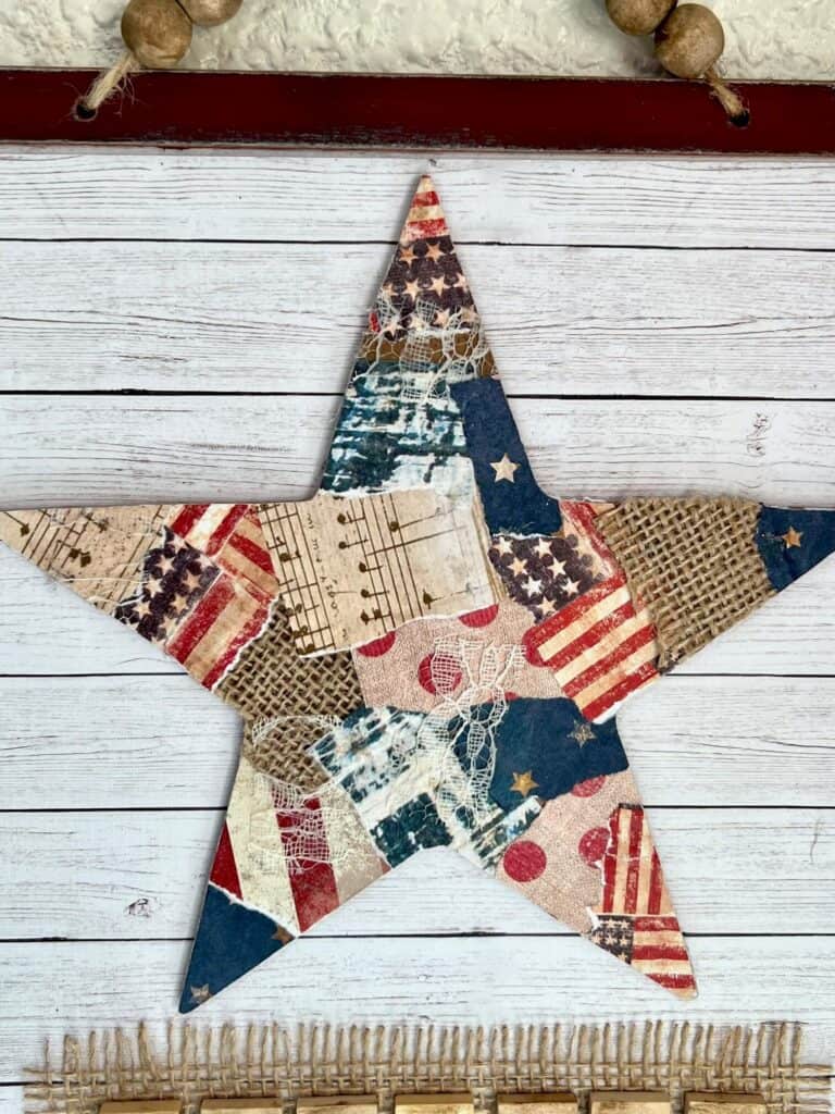 The wood patchwork star with patriotic scrapbook paper mod podged to the front with a shiplap background.