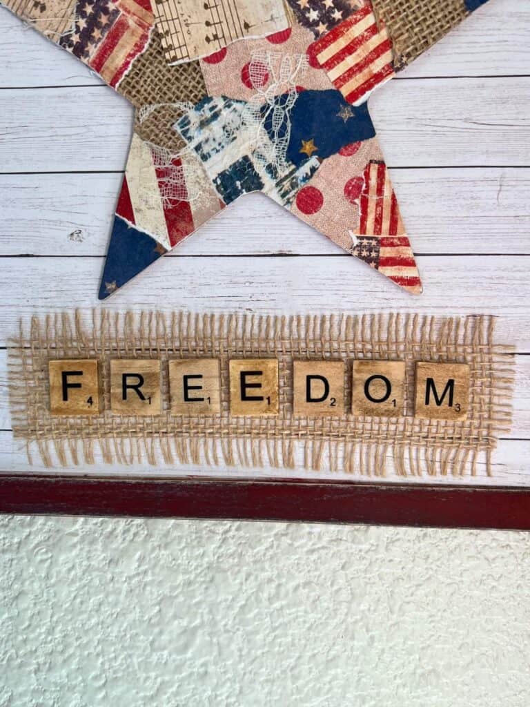 The word freedom in scrabble tiles glued under the star with a piece of burlap underneath.
