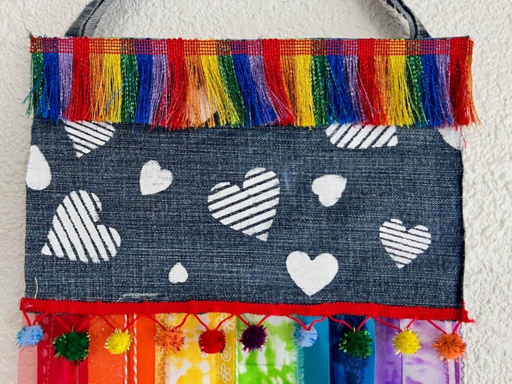 The top part of the denim flag with white stenciled hearts and rainbow fringe trim.