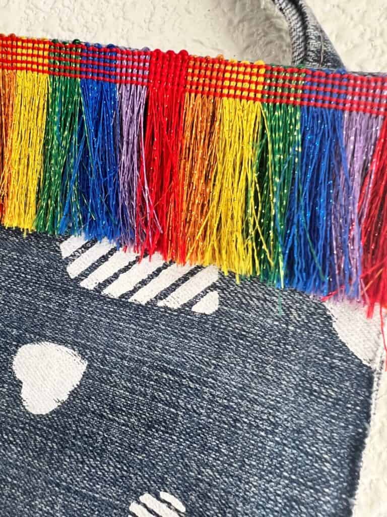 Rainbow sparkly fringe at the top of the denim piece.