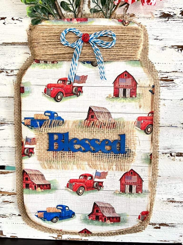 The wood mason jar with a patriotic red white and blue vintage truck napkin decoupaged to the front with a piece of burlap and the word blessed.