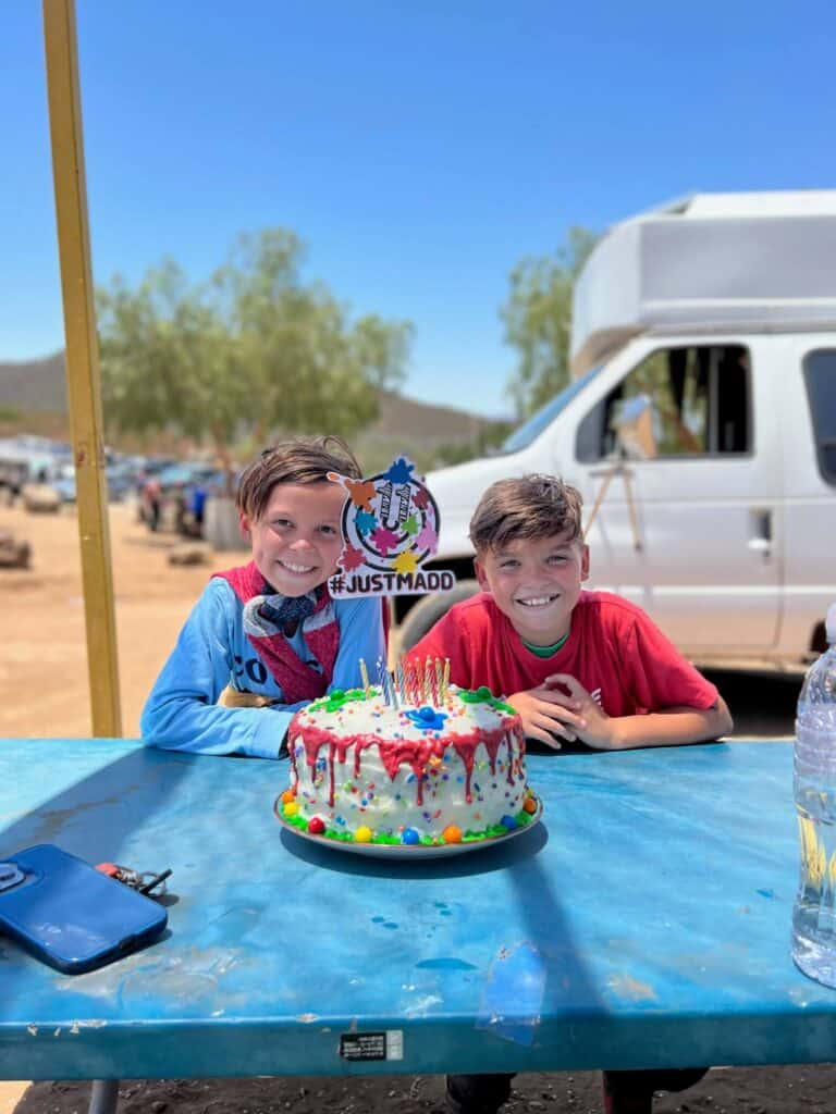 Twin boy sitting at a table with a Paintball themed cake sitting in front of them at their birthday party.