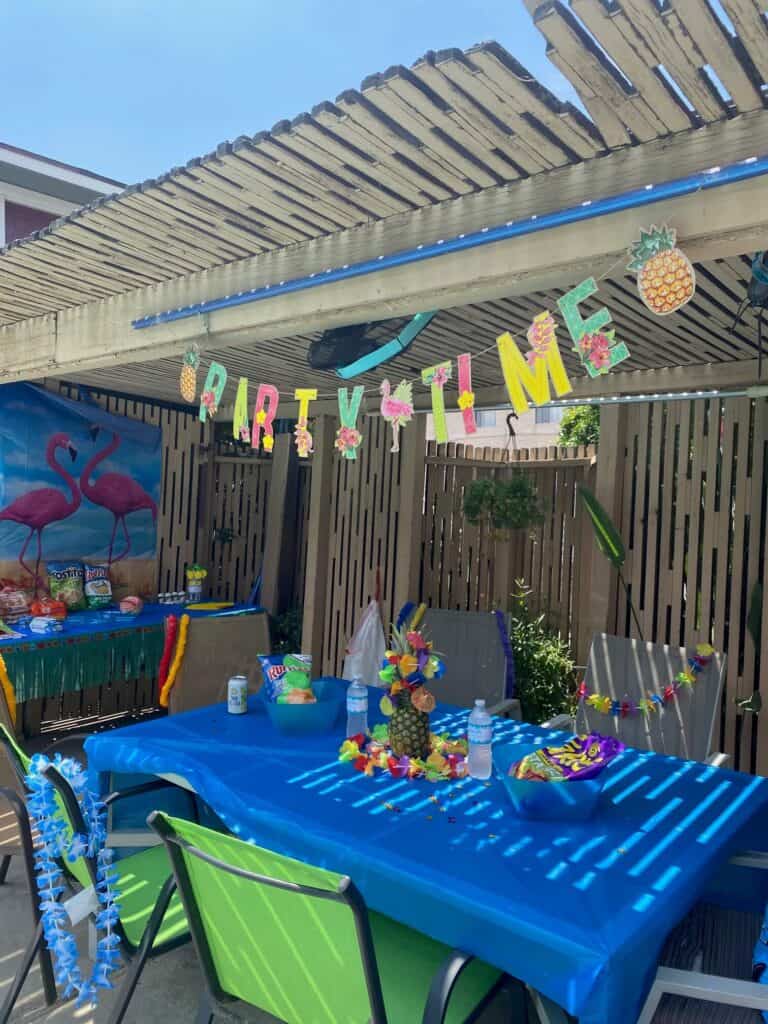 A Luau party set up with a banner that says "Party. Tie", a pineapple, aloha flowers, and flamingo backdrop.