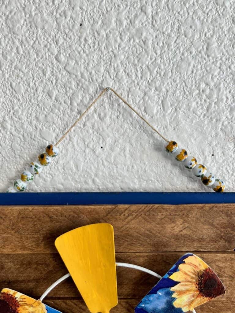 A twine hanger made of ceramic sunflower beads used to hang the completed project.