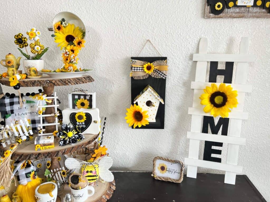 A sunflower tiered tray on the left, the DIY Birdhouse decor in the middle hanging on the wall, and a HOME Ladder to the right.