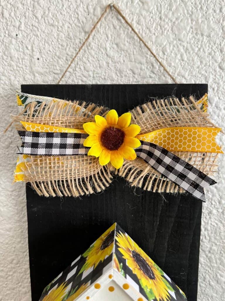 A small burlap and buffalo check bow with a sunflower in the center.