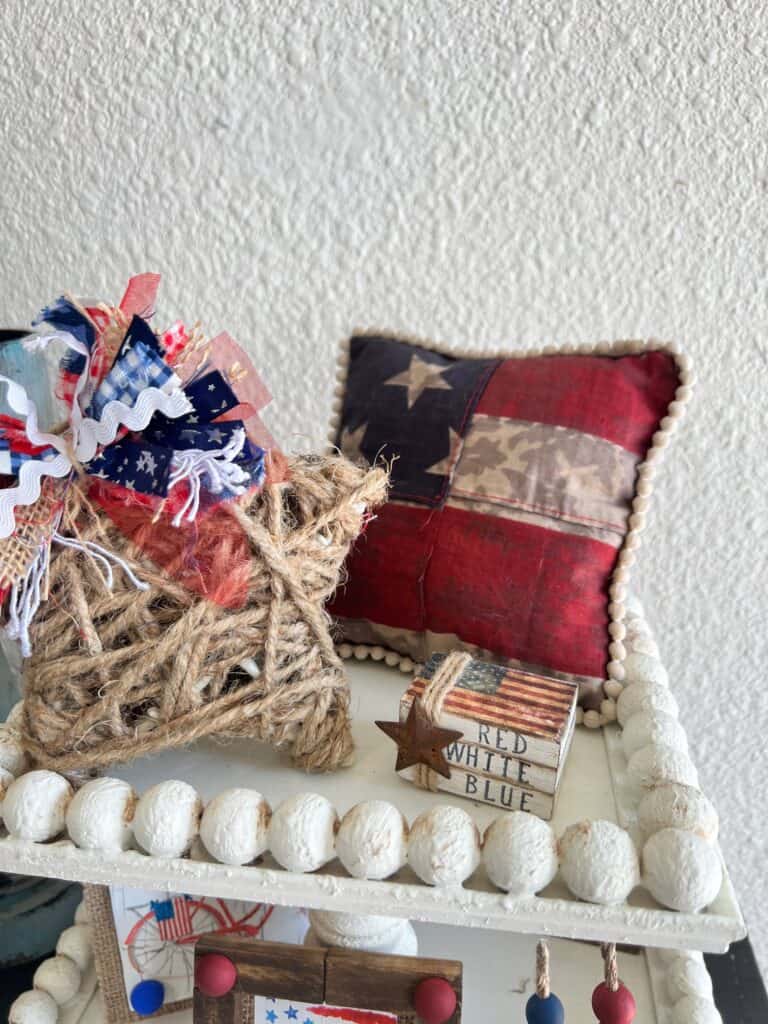 The vintage american flag mini bookstack sitting on top of a white tired tray with a twine star and a flag pillow.