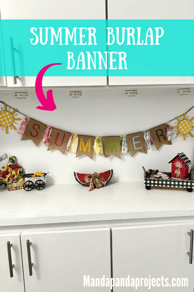 A crafty Summer burlap banner with colorful letters  stenciled on the burlap and fabric strips in between, a yellow sun on each end, hanging on a shelf decorated for summer.