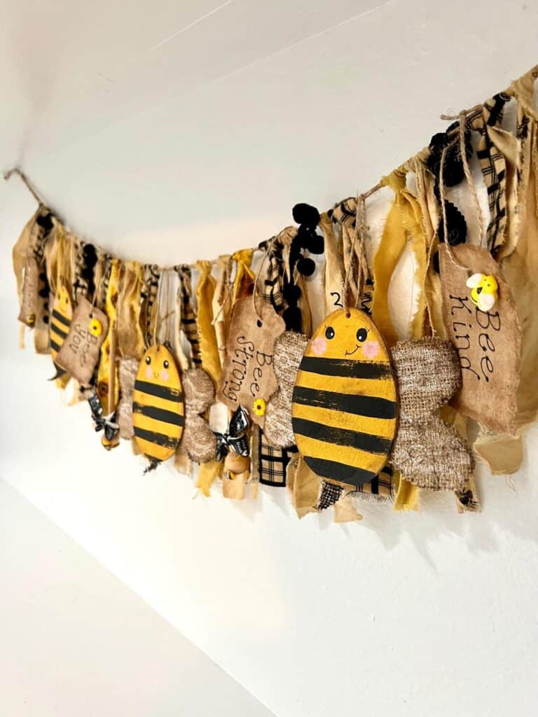 A distressed grungy style bee and sunflower swag made of fabric hanging on the wall.