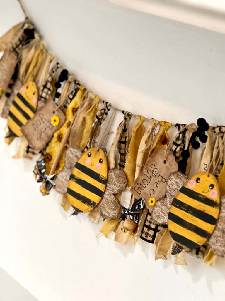 A distressed grungy style bee and sunflower swag made of fabric hanging on the wall.