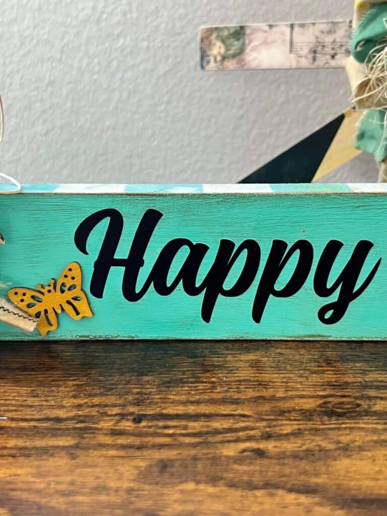 The word Happy cut from cricut black vinyl with a small yellow butterfly on the bottom left and a teal background.