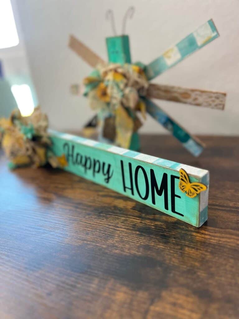 Portrait view of the right side of the long board showing the word HOME and a small yellow wooden butterfly, with the edges covered in Teal check rice paper.