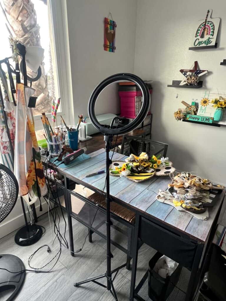 A large L-Shaped desk in front of a big window in a craft room covered in crafts and supplies.