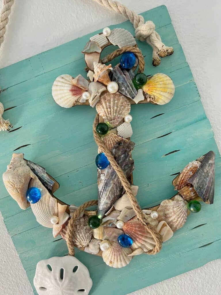 The wood anchor completely covered with seashells, pearls, and glass beads, with jute rope wrapped around it.