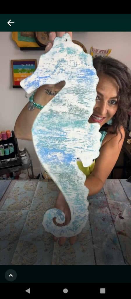 The surface of the seahorse with blue and green ombre background and white chippy paint on top of it giving it a distressed look.