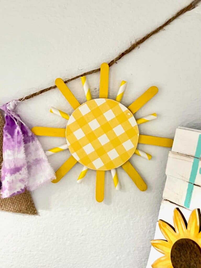 A yellow plaid sun with yellow and white popsicle sticks and paper straws as the suns "rays".