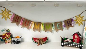 A crafty Summer burlap banner with colorful letters stenciled on the burlap and fabric strips in between, a yellow sun on each end, hanging on a shelf decorated for summer.