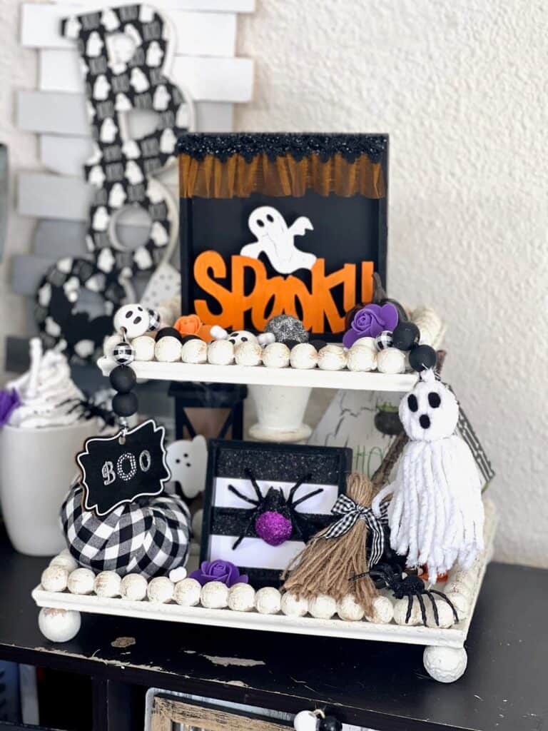 The white tiered tray with a shelf sitter that has a ghost and the word "spooky" painted orange. The bottom of the tray is also decorated with carious Halloween decor.